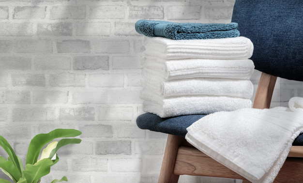 Clean terry towels on wooden chair with brick wall background, c